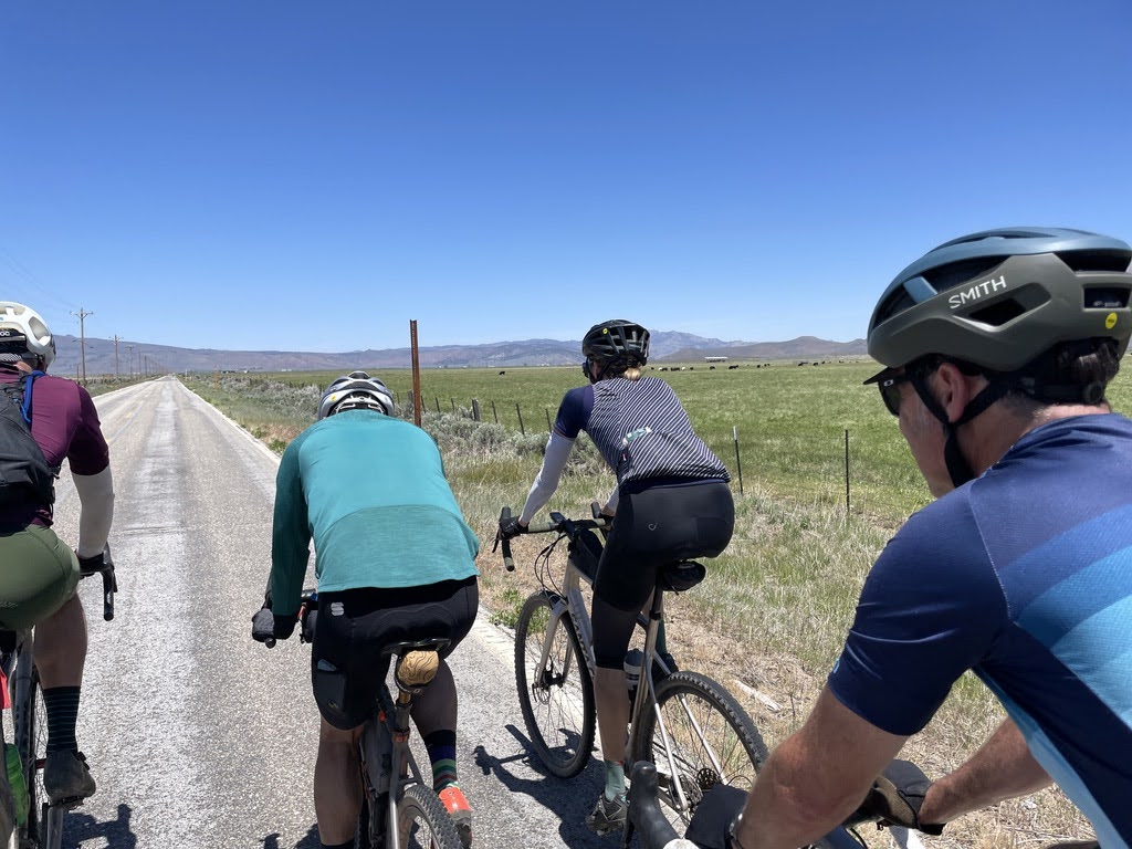 Gravel cyclists riding an open road through a wide valley with blue skies
