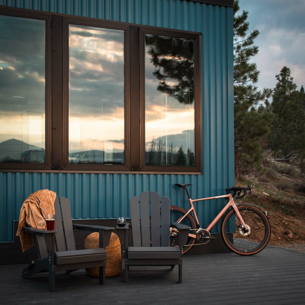 Gravel bike parked beside Adirondack chairs on a cabin deck at dusk with mountain views