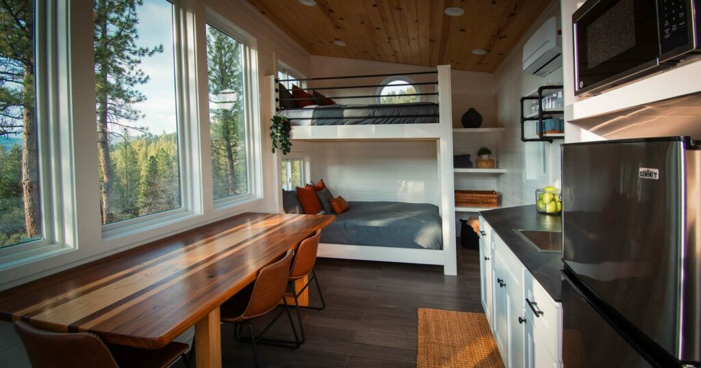 Interior of the High Camp cabin showing bunk beds, full kitchen, and forest views through large windows