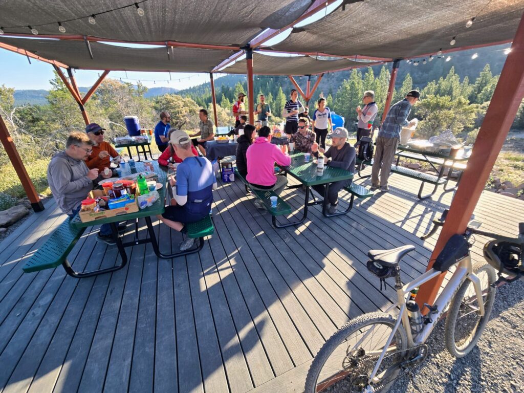 Gravel Social riders eating breakfast under the covered deck at High Camp